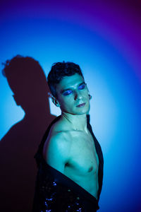 Gay man with eyeshadow posing eyes closed against illuminated background