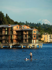 Man paddleboarding on lake with buildings in background