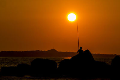 Silhouette man sitting on rock against sky during sunset