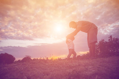 Friends standing on field against sky during sunset