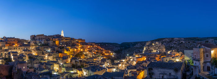 Illuminated buildings in city against clear blue sky