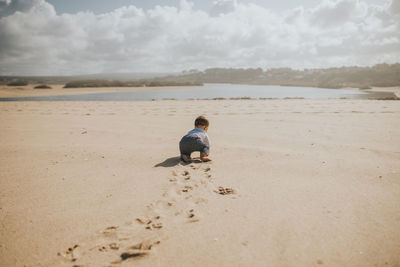 Rear view of cute boy on beach against sky