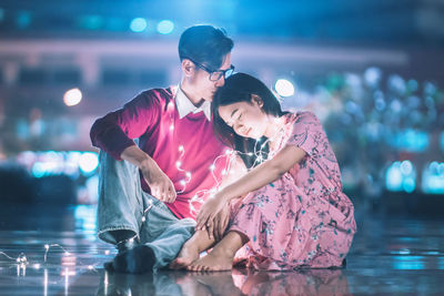 Mother and daughter sitting in illuminated water at night