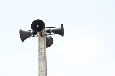 Low angle view of megaphones on pole against blue sky