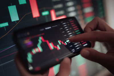 Hand of young business girl looking at trading graphs on office computer and mobile phone