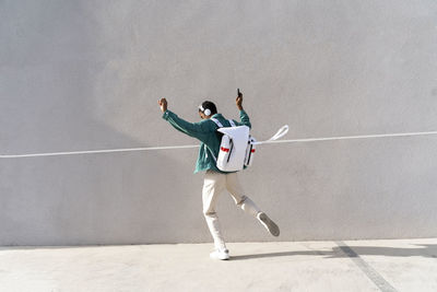 Full length of man with arms raised standing against wall