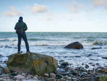 Man standing on rock in the middle of ocean. tourist stand alone on a rock and watching sea horizon