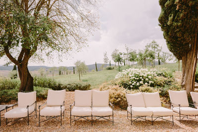 Empty chairs and tables by trees against sky