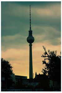 Low angle view of communications tower against cloudy sky