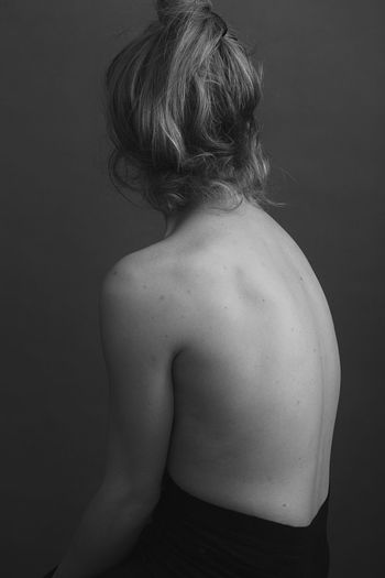 REAR VIEW OF SHIRTLESS MAN LOOKING AWAY AGAINST GRAY BACKGROUND