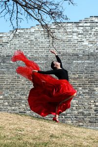 Full length of woman dancing on field against brick wall