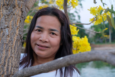 Portrait of smiling woman against tree trunk