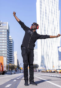 Man with arms outstretched listening to music standing against building in city