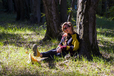 Young woman sitting on tree trunk in field
