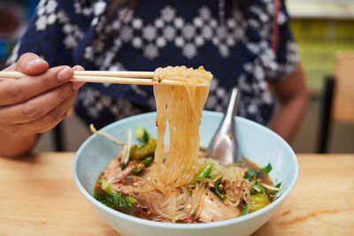 Woman hand uses bamboo chopsticks to pickup rice stick noodles for eating