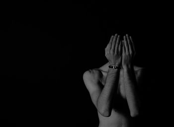 Shirtless man covering face with hands against black background