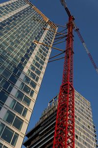 Low angle view of crane by building against sky