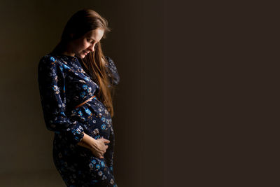 Stunning pregnant woman, young expecting mother to be on a black background, studio photography