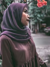 Smiling young woman looking away while standing against trees