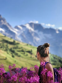 Rear view of woman on purple flowering plants against sky