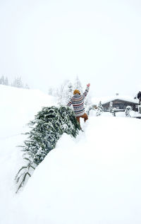 Man coming home, waving and pulling christmas tree in the snow