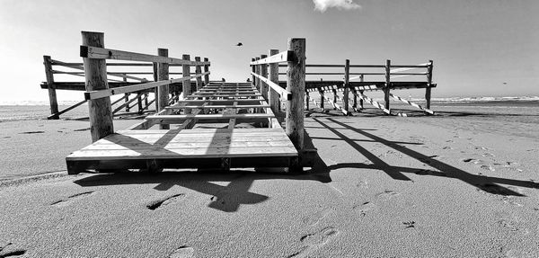 Empty bench on beach against sky