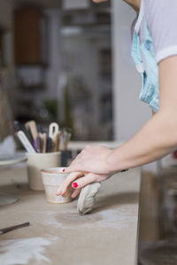 Midsection of female potter kneading clay on workbench at store