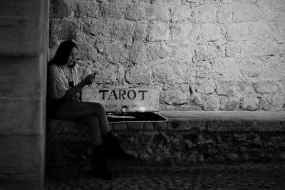 Side view of woman sitting against wall