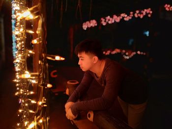 Side view of young woman looking at illuminated christmas lights