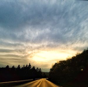 Road amidst trees against sky during sunset