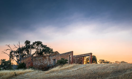 Abandoned building on field against sky during sunset