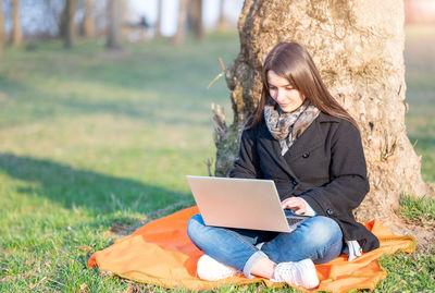 Woman using laptop while sitting on field