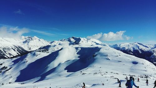 People on snow covered land against mountains and blue sky