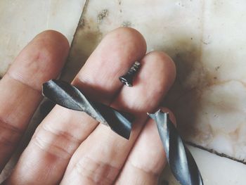 Cropped hand holding broken screw over table