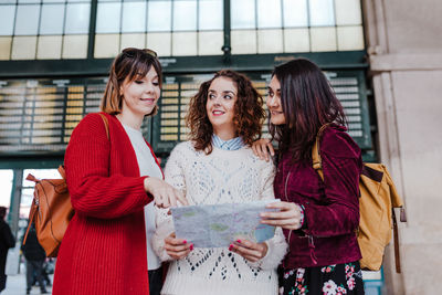 Cheerful women holding map while standing outdoors