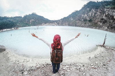 Rear view of woman with arms outstretched standing against lake