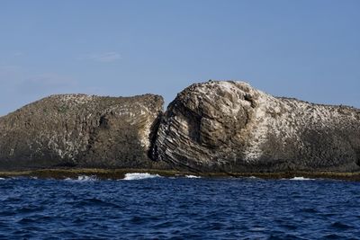 Rock formation in sea against clear blue sky