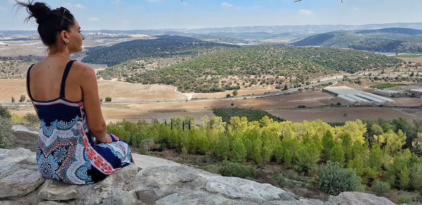 Woman sitting on rock against landscape and sky