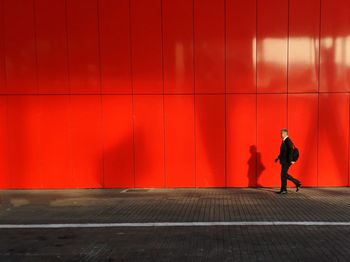 Full length of man walking on sidewalk against red wall