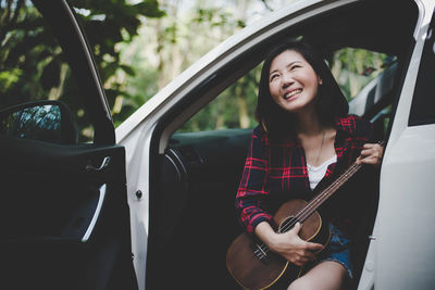 Happy mid adult woman playing ukulele in car