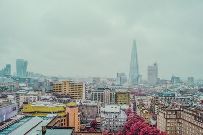 Cityscape by shard against sky during foggy weather