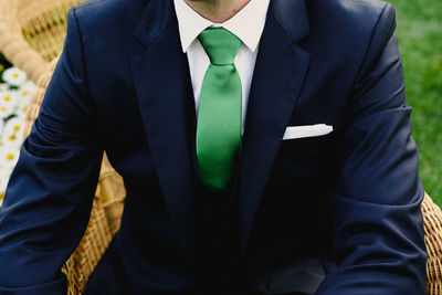 Midsection of bridegroom sitting on seat during wedding ceremony