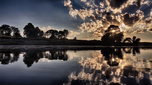 Silhouette trees by lake against sky during sunset