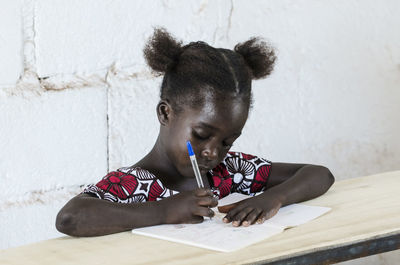 Portrait of girl sitting on table against wall