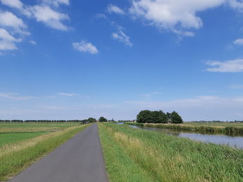 Empty road amidst field against sky