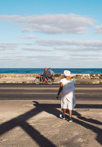 People riding bicycle by sea against sky