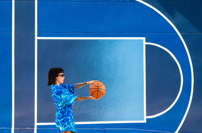 Caucasian girl with sunglasses and tattoos on a blue background with a basketball