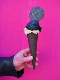 Hand holding ice cream cone against pink wall