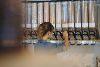 Businesswoman filling grain in glass jar while standing in cafe