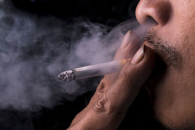 Cropped image of man smoking cigarette against black background